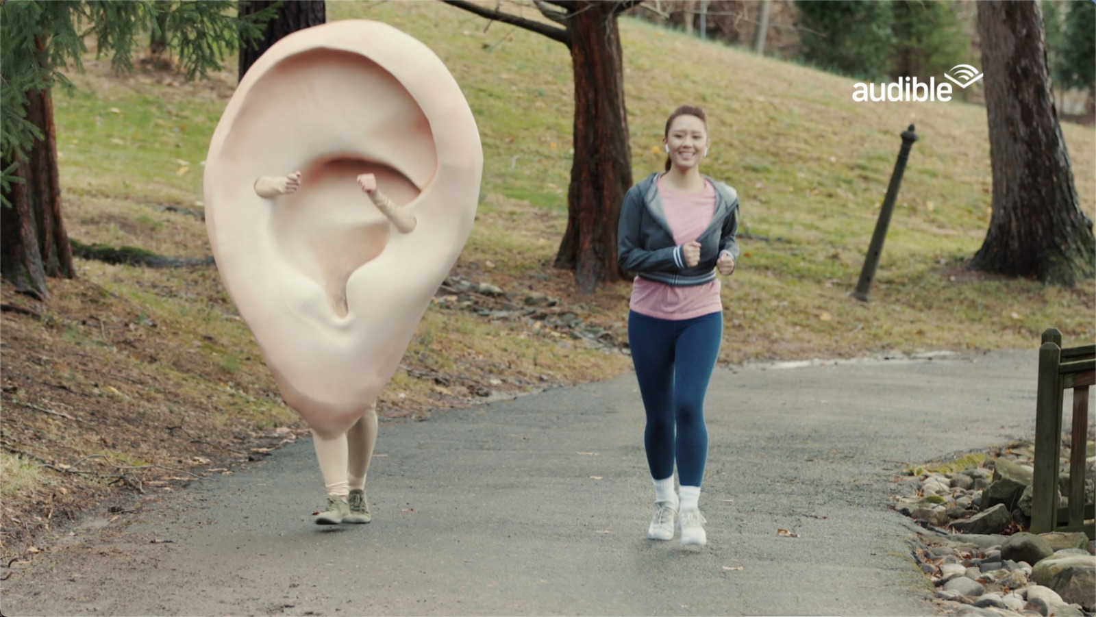 A woman jogging past a giant sculpted ear in a park, from an Audible commercial